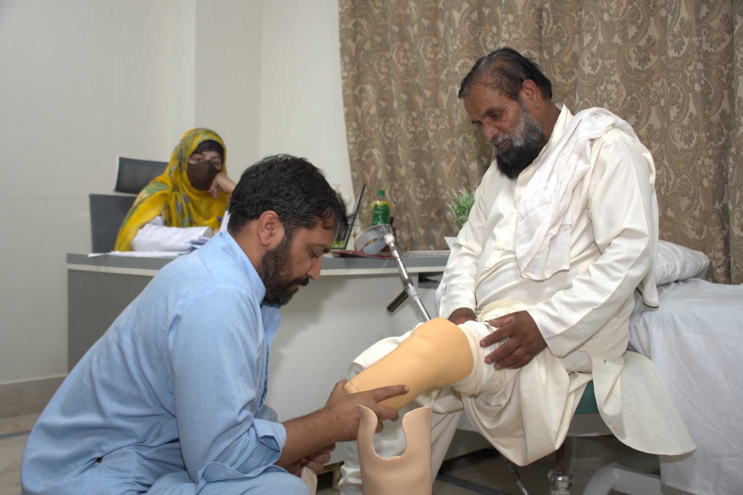 A prosthetist fitting an elderly patient with a new above-knee prosthetic leg at an HHRD rehabilitation center